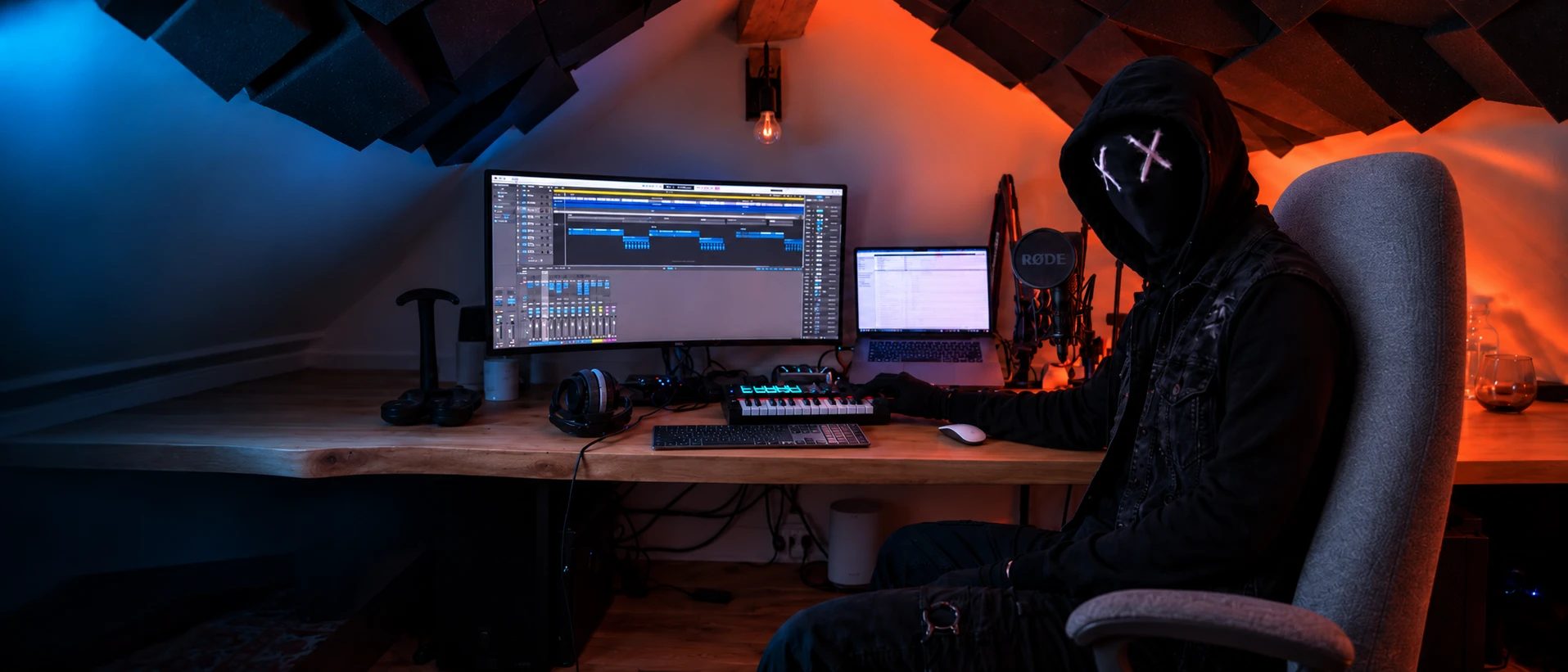 Aatom dans son studio sous les néons, cagoule noire et X peints sur les yeux